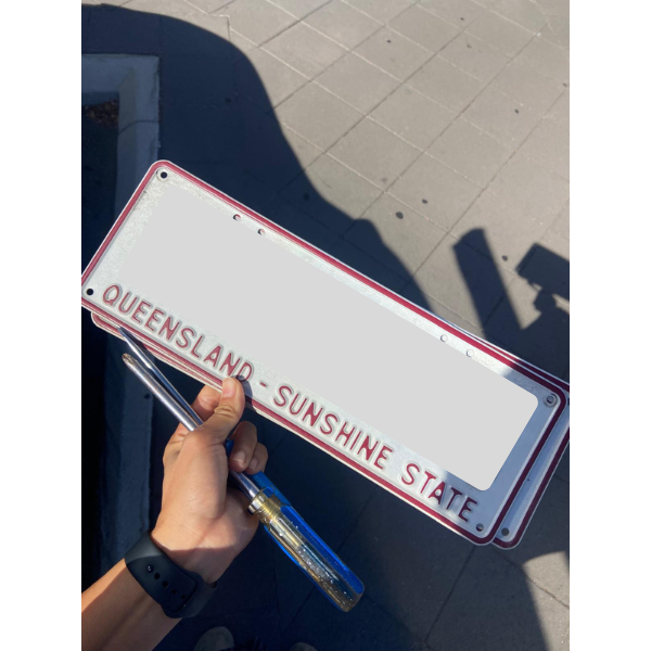 Queensland（クイーンズランド）のナンバープレートを手に持って返却しに行く様子。赤い縁とSUNSHINE STATEの文字が入ったプレートを外した状態で写っている